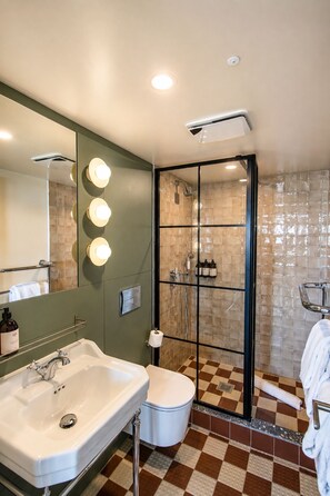 A bathroom with a large mirror, two sinks, a toilet, and a shower with a glass door.