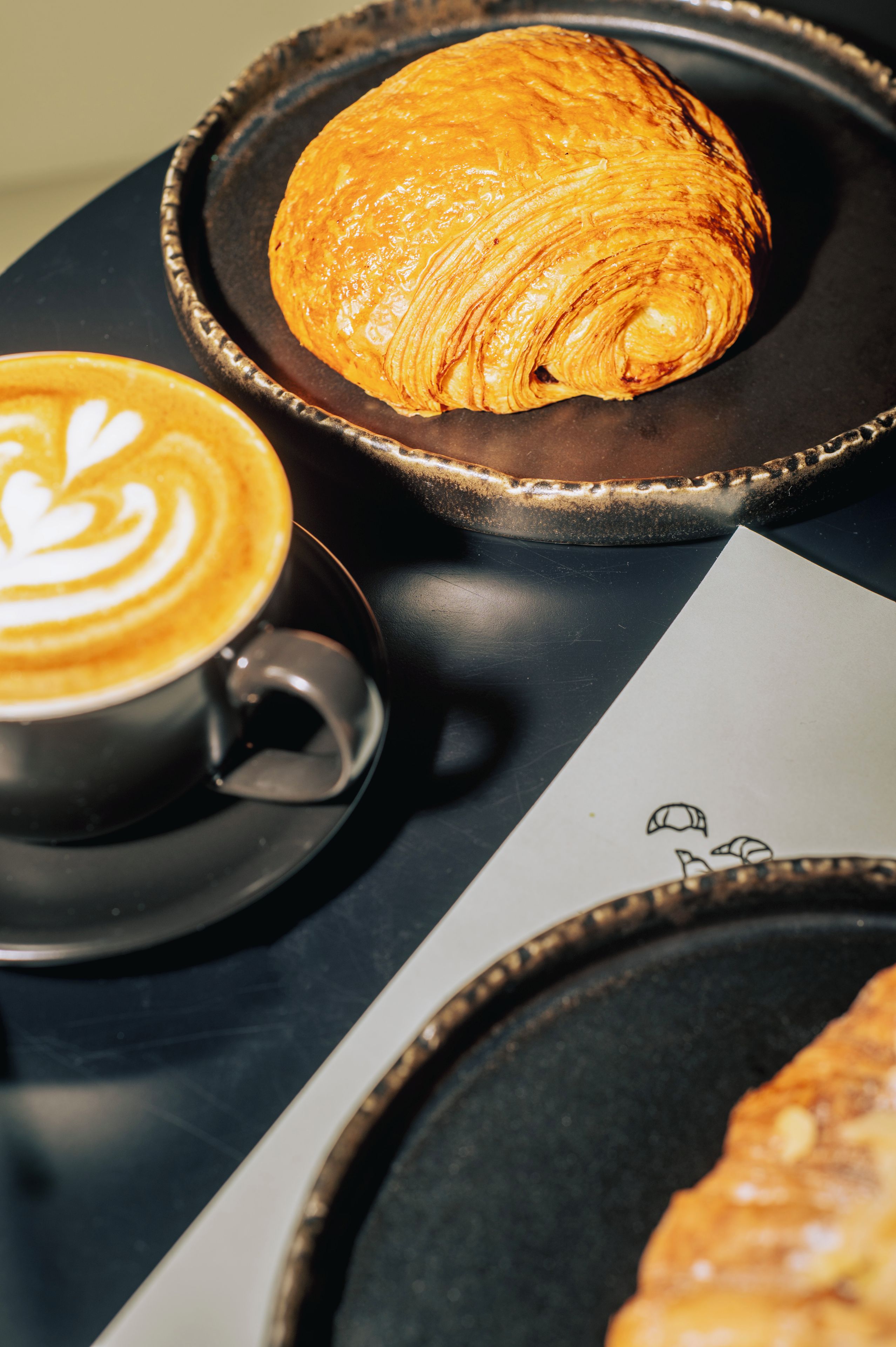 A table with a croissant, a cup of coffee, and a menu.