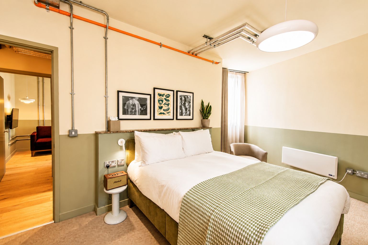 Ein Hotelzimmer mit Bett, Nachttisch, Lampe, gerahmten Bildern und Blick auf den Flur.