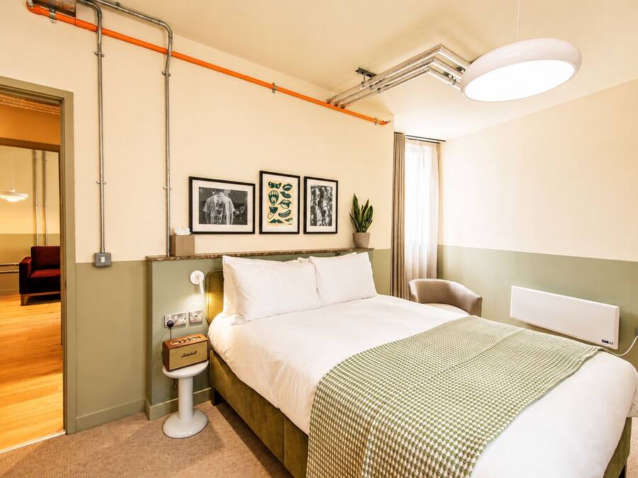 Ein Hotelzimmer mit Bett, Nachttisch, Lampe, gerahmten Bildern und Blick auf den Flur.