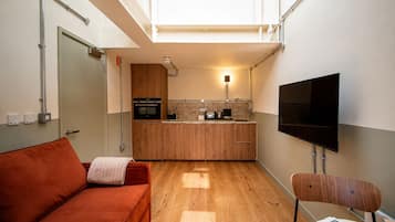 A compact living space with a kitchenette, a sofa, a television, and a chair.