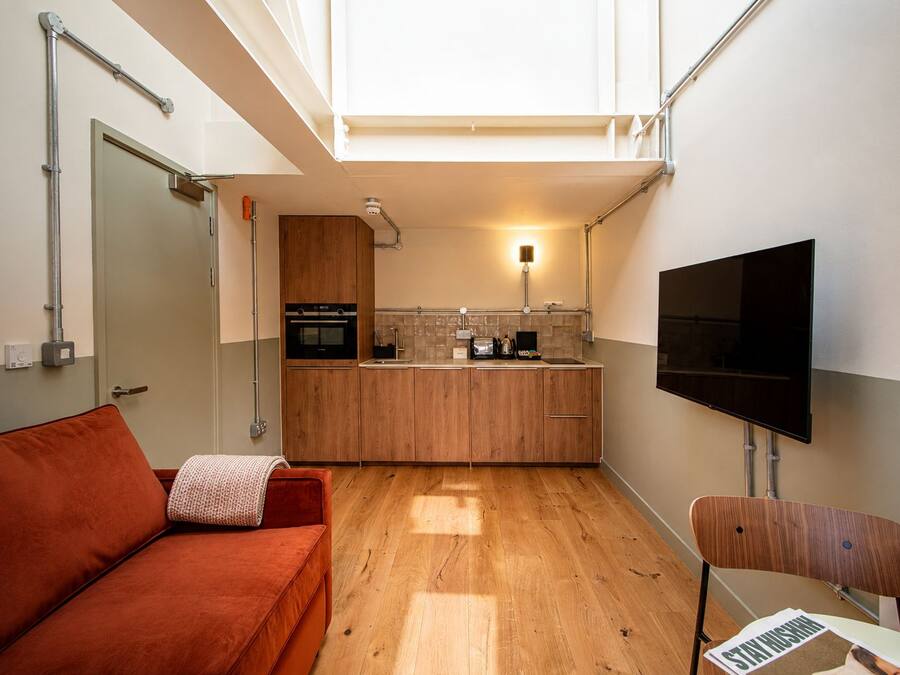 A compact living space with a kitchenette, a sofa, a television, and a chair.