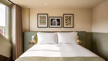 Hotelkamer met een groot bed, een hoofdeinde, een raam met gordijnen en drie ingelijste foto’s aan de muur.