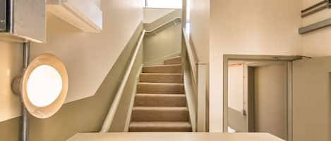 A staircase with carpeted steps leading to a landing, a light fixture on the wall, and a door with a handle.