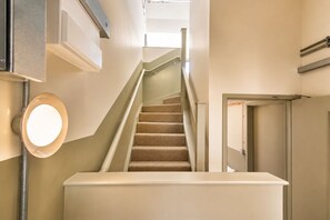 A staircase with carpeted steps leading to a landing, a light fixture on the wall, and a door with a handle.