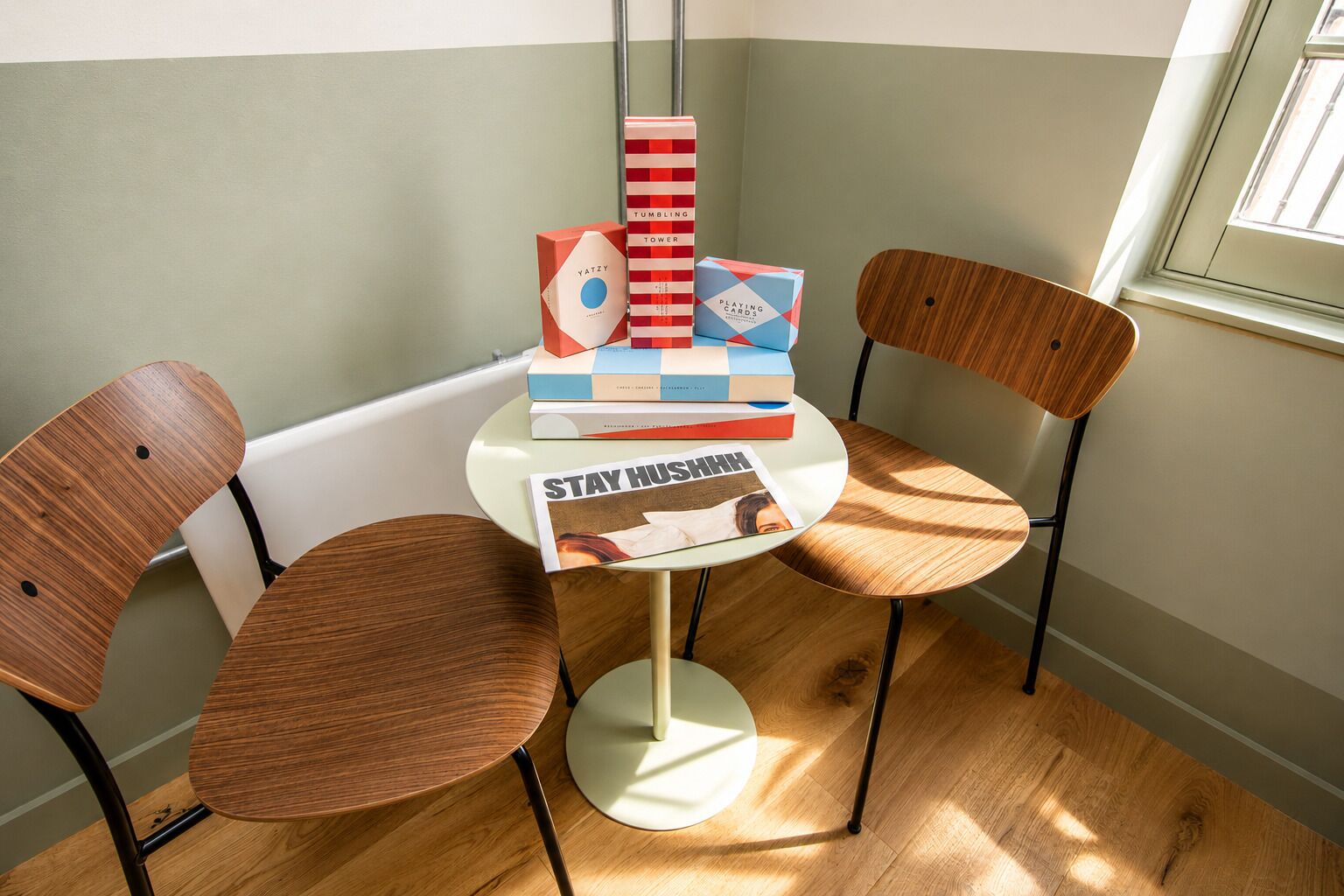 A corner room with a round table, two wooden chairs, and a window.