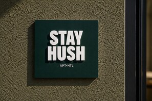 A sign with the text 'STAY HUSH' and 'APT. HTL' on a textured wall. - Stay Hush (Edinburgh)