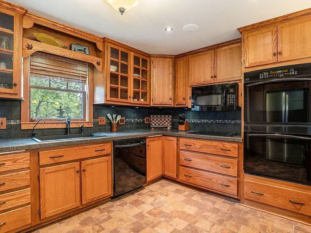 A kitchen with wooden cabinets, a microwave, an oven, and a window with blinds.