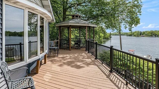 Une terrasse en bois avec un belvédère, des sièges d’extérieur et une vue sur un lac.
