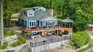 Une maison à deux étages avec une terrasse, entourée d’arbres.