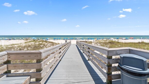 Een houten looppad dat naar een strand leidt, met parasols en strandstoelen.
