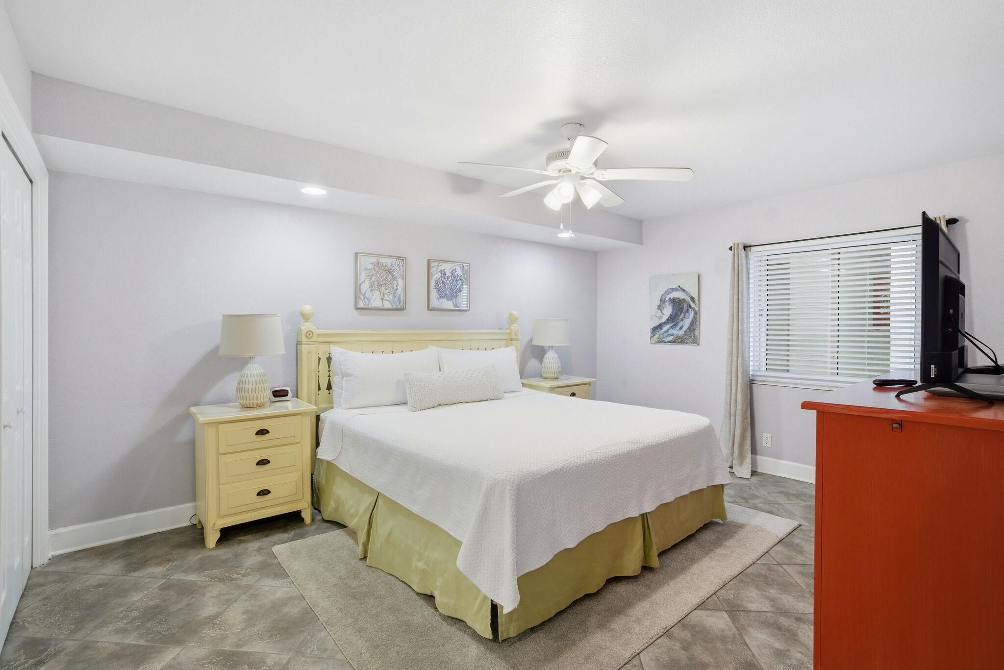 Un dormitorio con cama, mesitas de noche, escritorio y ventilador de techo.