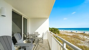 Een balkon met Adirondack-stoelen, een tafel en uitzicht op het strand en de oceaan.