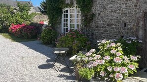 A stone building with a tiled roof, a gravel driveway, and potted plants with pink flowers. - A haven of peace just a few minutes from the sea, ideal for families (Montmartin-sur-Mer)