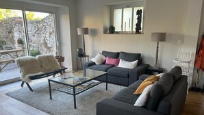 A modern living room with a glass coffee table, two sofas, a wicker chair, and a stone wall. - A haven of peace just a few minutes from the sea, ideal for families (Montmartin-sur-Mer)