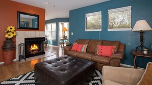A living room with a fireplace, leather sofa, ottoman, and a ceiling fan. - Cozy 1-bedroom condo, in soothing Tucson with fitness room, pools & trails (Tucson)