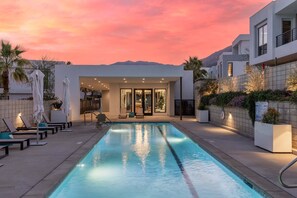 A swimming pool with lounge chairs and umbrellas, a modern building with a glass door entrance, and a mountainous backdrop. - Cody Place Luxe–Palm Springs Contemporary Home w/ Resort Amenities, Mountain Views & Downtown Access (Palm Springs)