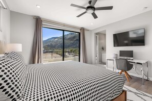 Ein Schlafzimmer mit Bett, Schreibtisch mit Computer, Fernseher und Balkon mit Bergblick.