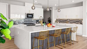 Una cocina moderna con armarios blancos, una isla de mármol y sillas de alambre doradas.