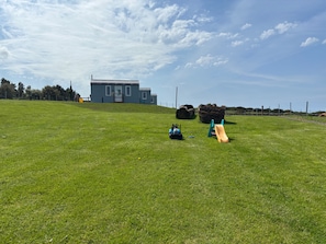 Um campo gramado com uma casa pequena, uma rocha grande e um carrinho de brinquedo.