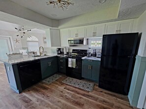 Una cocina moderna con armarios oscuros, un refrigerador negro, un microondas y una estufa. El piso es de madera y hay una alfombra estampada.