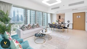 A modern living room with a sofa, coffee table, and dining area. - Vogue | Downtown with Direct Access to Dubai Mall (Dubai)