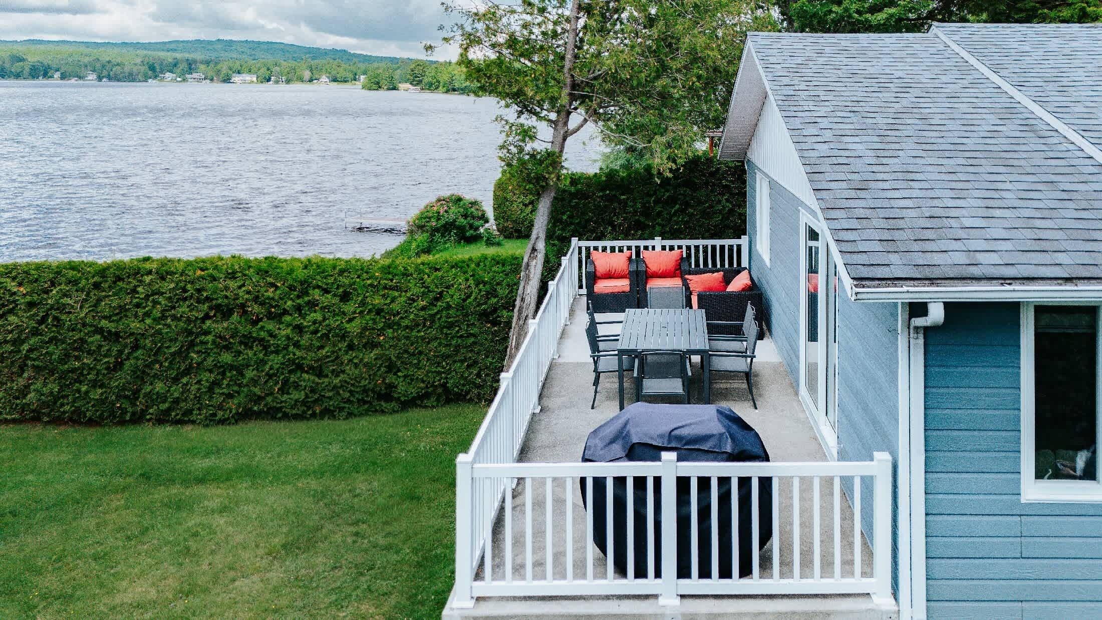 A house with a deck overlooking a lake, featuring outdoor furniture and a clear view of the water.