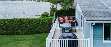 A house with a deck overlooking a lake, featuring outdoor furniture and a clear view of the water.