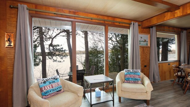A room with two armchairs, a small table, and a view of trees through large windows. - Little Glen Lake 3 bedroom, 2 bath, Air Conditioning, Great Swimming & Fishing (Empire)