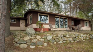A modern house with a stone retaining wall, large windows, and outdoor seating. - Little Glen Lake 3 bedroom, 2 bath, Air Conditioning, Great Swimming & Fishing (Empire)