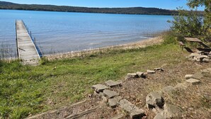 A wooden dock extending into a calm lake, surrounded by grassy areas and a picnic table. - Little Glen Lake 3 bedroom, 2 bath, Air Conditioning, Great Swimming & Fishing (Empire)
