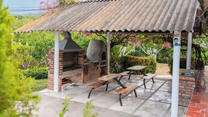 Eine Terrasse im Freien mit einem Backstein-Barbecue, Picknicktischen und einem Metalldach.