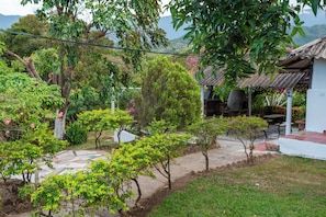 A garden with a patio area, a small building with a corrugated metal roof, and a view of hills in the background. - Private 2-bedroom farmhouse in Santa Marta with stunning views. (Santa Marta)