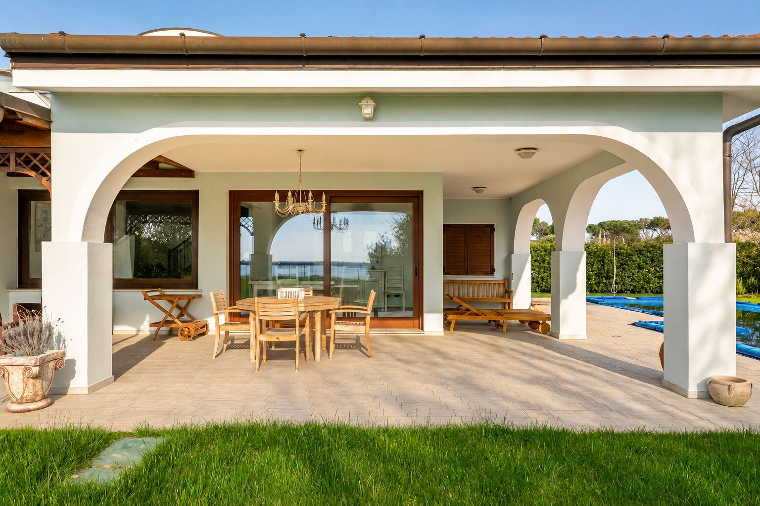 Eine überdachte Terrasse im Freien mit Esstisch und Stühlen, einem Pool und Blick auf das Meer.