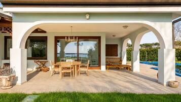 Eine überdachte Terrasse im Freien mit Esstisch und Stühlen, einem Pool und Blick auf das Meer.