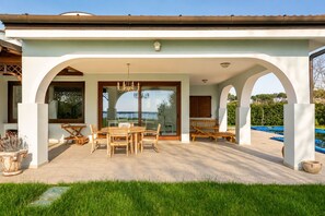 Un porxo exterior cobert amb taula i cadires, piscina i vistes al mar.