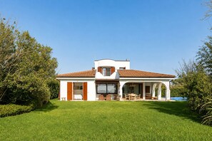 Une maison à deux étages avec un patio couvert, une pelouse et un ciel bleu dégagé.