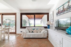 A living room with a sofa, TV, and a dining area with chairs and a table.