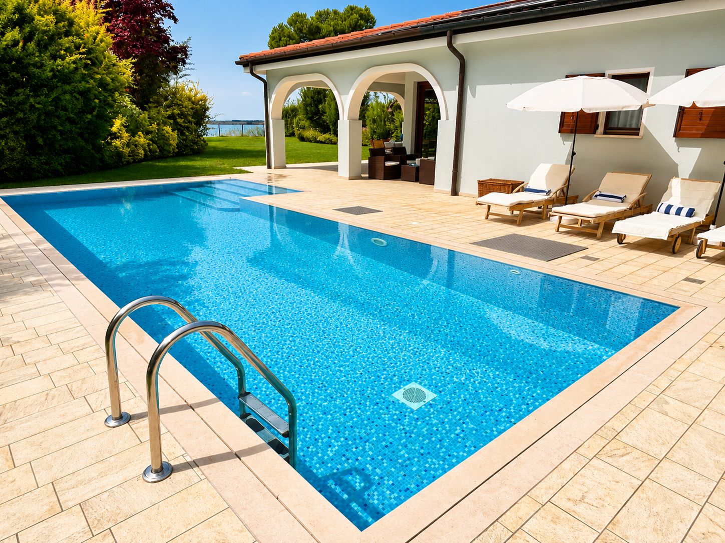 A swimming pool with a clear blue water, surrounded by a tiled deck, and a lounge area with chairs and umbrellas.