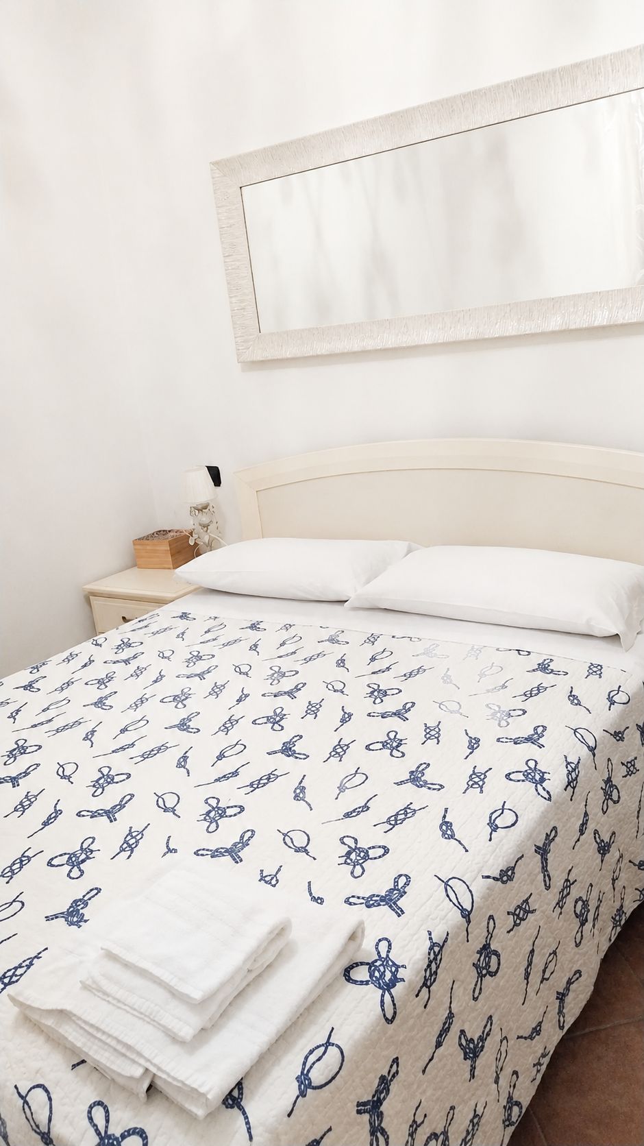 Un lit avec une tête de lit blanche, une couvre-lit à motifs et des serviettes blanches soigneusement pliées au pied du lit.