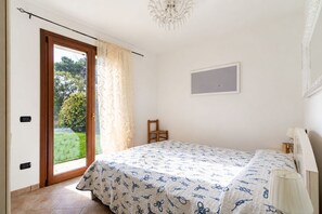 Une chambre à coucher avec un lit, une chaise, une fenêtre avec des rideaux, un lustre et un tableau encadré accroché au mur.