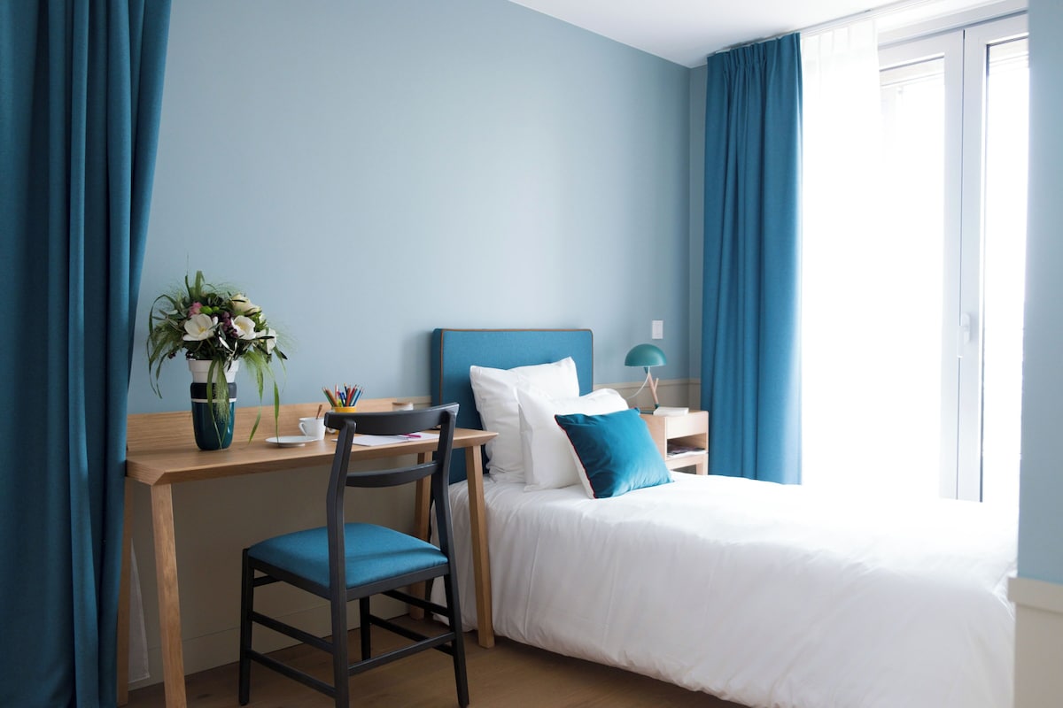 Une chambre à coucher avec un lit, un bureau, une chaise et une table de chevet.