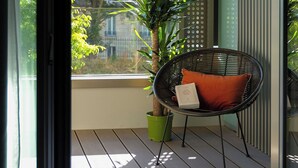 A balcony with a chair, a potted plant, and a view of buildings. - Zenao Appart'hôtels Auteuil (Paris)
