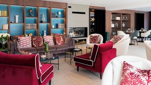A modern living room with a sofa, armchairs, a coffee table, and a TV. There are bookshelves with decorative items and a fireplace. - Zenao Appart'hôtels Auteuil (Paris)