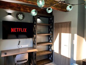 A room with a TV displaying 'NETFLIX', a wooden desk, a chair, a bookshelf, and a door. - Modern Wood Loft | 7 Min to Colonnade (Karlovy Vary)