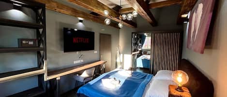 Une chambre d’hôtel moderne avec un grand lit, un bureau, un téléviseur diffusant « NETFLIX » et un plafond en bois.