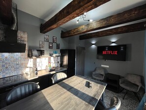 A modern kitchen with a wooden ceiling, a dining area with a table and chairs, and a wall-mounted TV displaying "NETFLIX". - Modern Wood Loft | 7 Min to Colonnade (Karlovy Vary)
