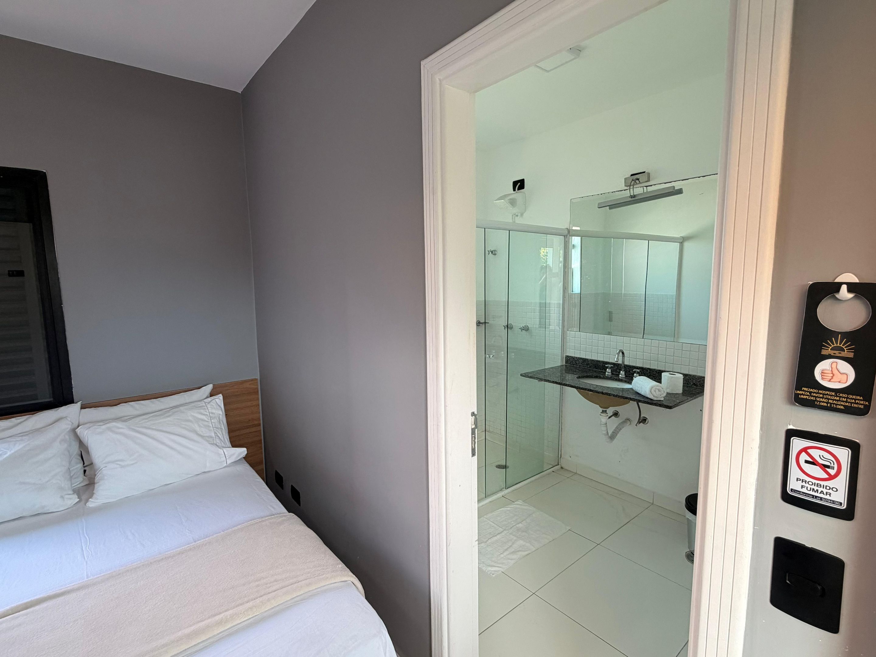 Quarto de hotel com cama, banheiro com box de vidro e toalha no chão.