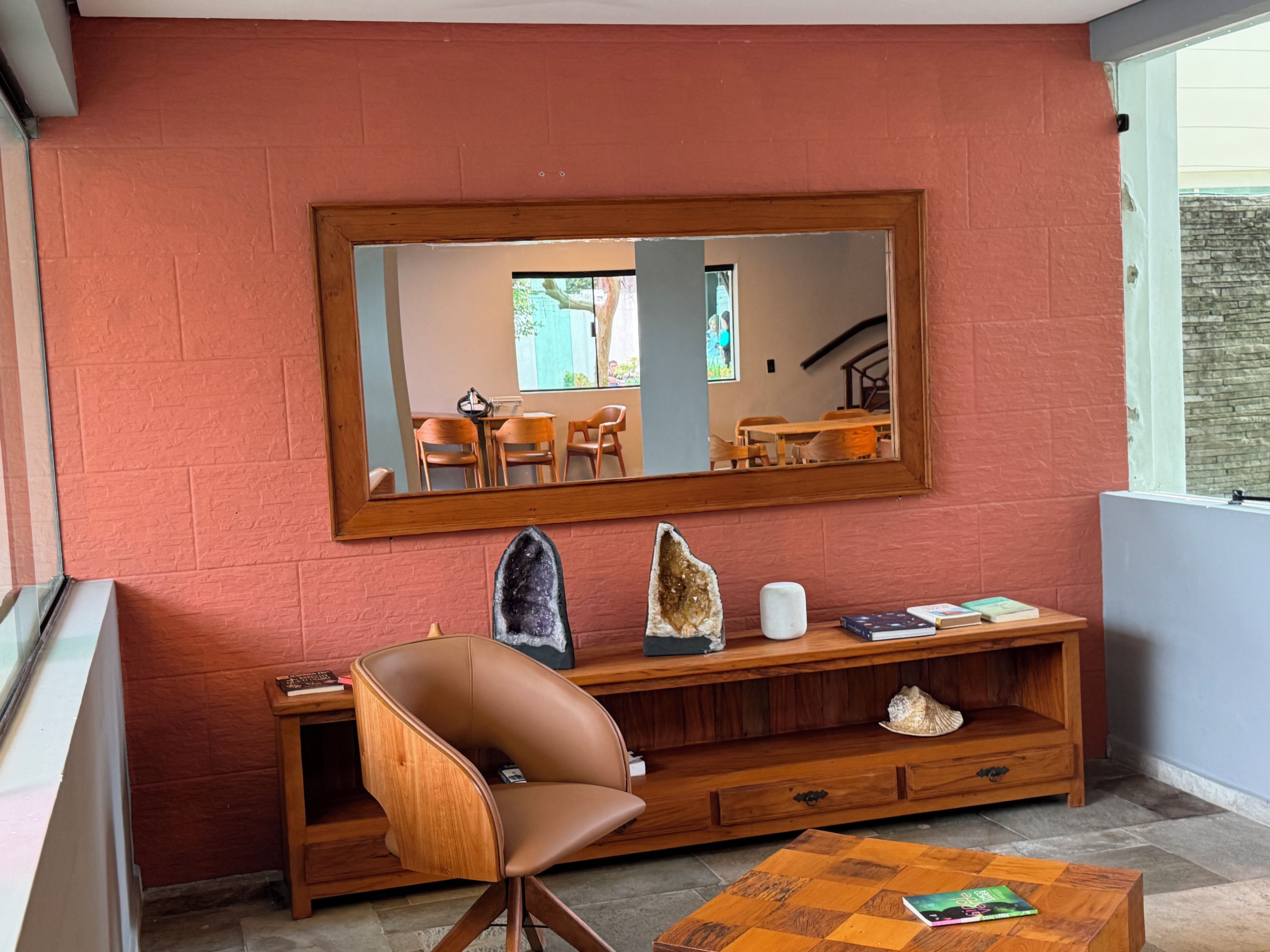 Una habitación con un espejo grande, una consola de madera, un sillón de cuero marrón y una mesita de centro pequeña.