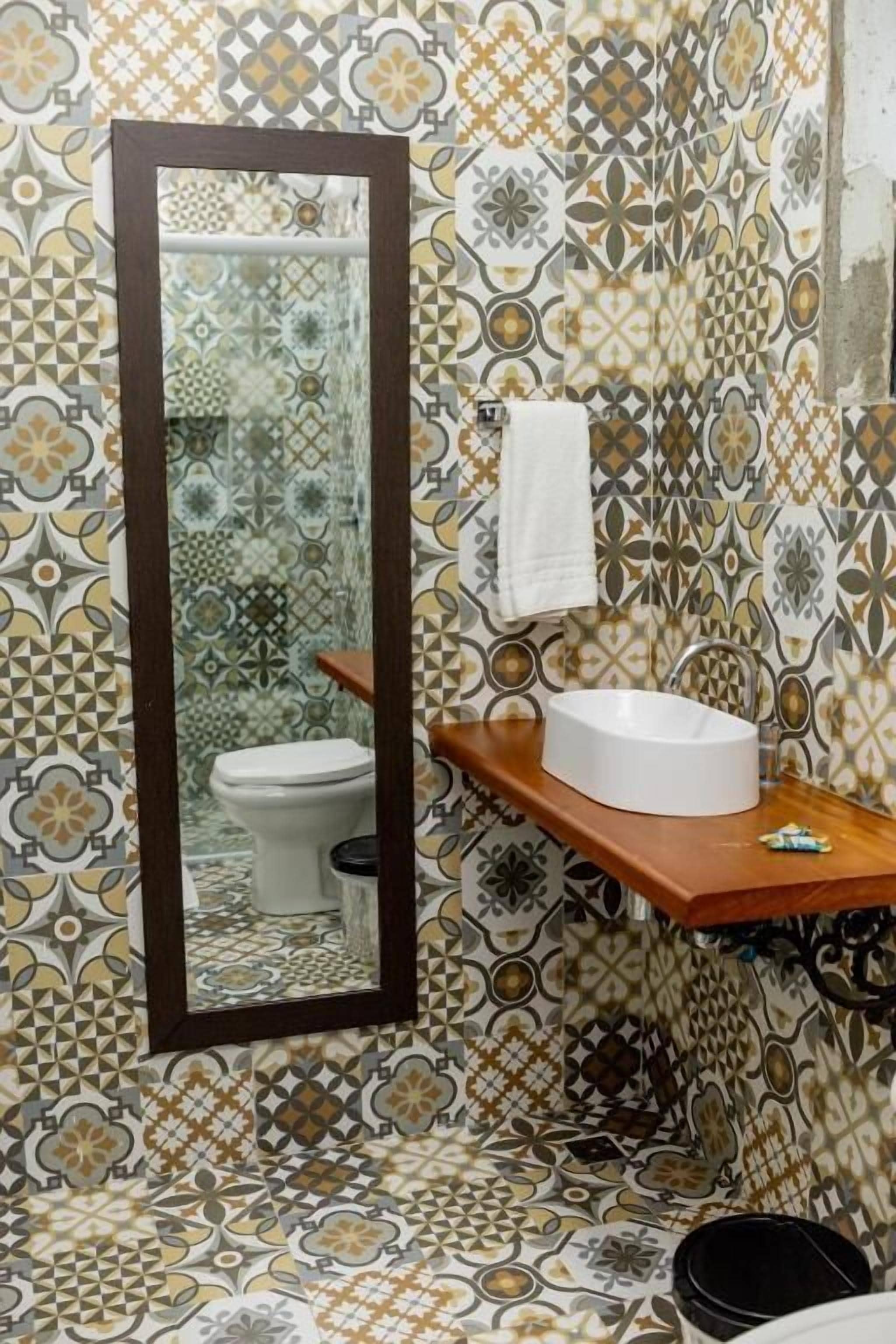 A bathroom with patterned tiles, a wooden vanity with a sink, a mirror, and a toilet.